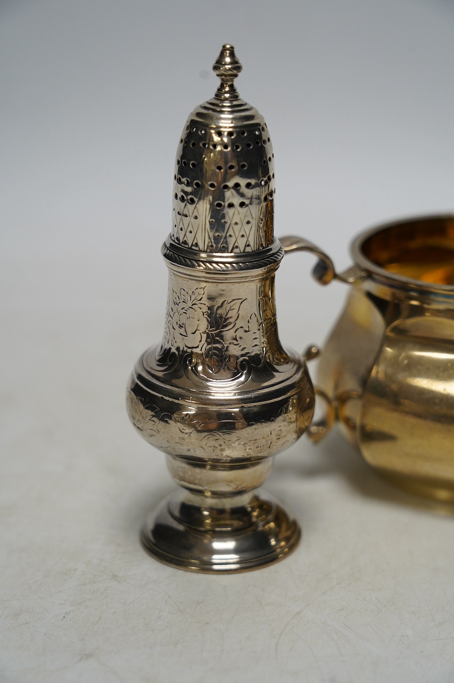 A George V silver two handled sugar bowl, Edward Barnard & Sons Ltd, London, 1926, two silver cream jugs including mounted glass and a white metal pepperette. Condition - poor to fair